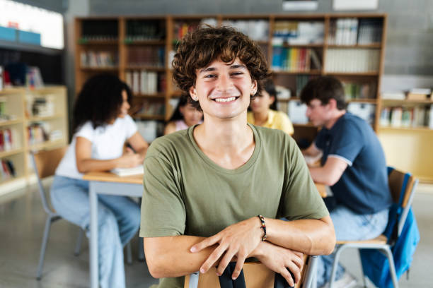 istock Young high school student man smiling at camera at library 2183646672