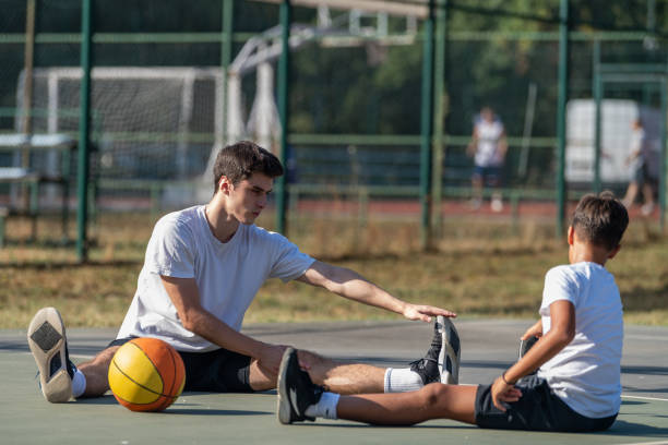 istock Young boy stretches with his coach during basketball training, focusing on flexibility and preparation. This outdoor session highlights foundational skills and active, healthy habits for youth. 2183654640