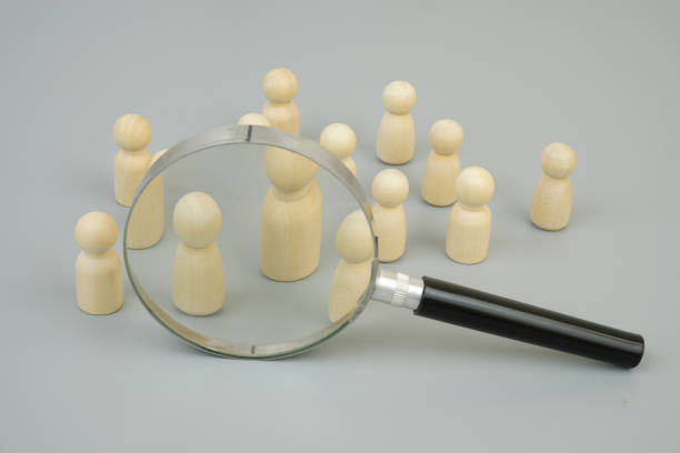 istock Wooden figures and magnifying glass on gray background. 2183657321