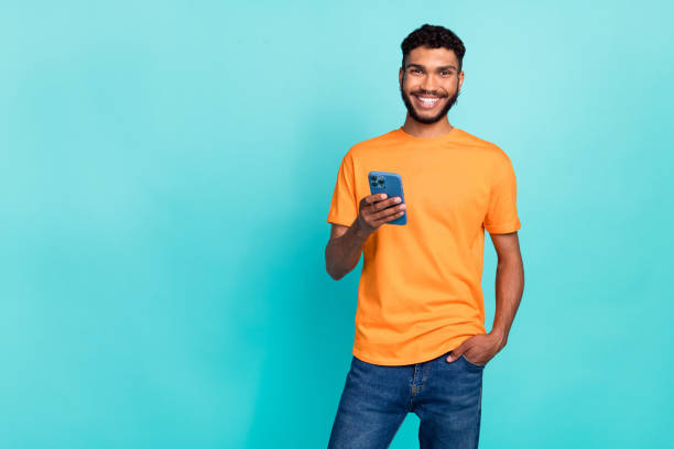 istock Photo of confident attractive man dressed orange t-shirt typing sms modern device empty space isolated turquoise color background 2183658492