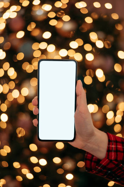 istock Close-up smartphone with empty screen mockup on holiday background with Christmas tree, customer holding phone in hand 2183664825