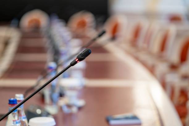 istock Microphone on a conference table with blurred chairs and water bottles in the background 2183665848