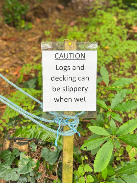 istock Image of 'Caution logs and decking can be slippery when wet' sign post, typed, printed and laminated restricted area sign, wooden stake, rope tied with knot, focus on foreground 2183682086