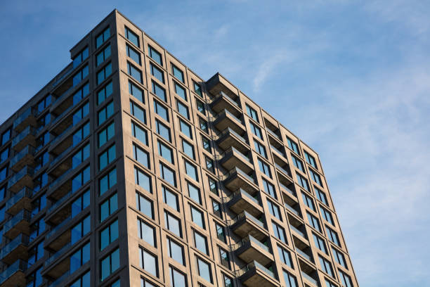 Close-up view of a modern high-rise apartment building with clean architectural lines and rows of balconies, set against a clear blue sky. Captures urban living and contemporary design in a metropolitan setting.