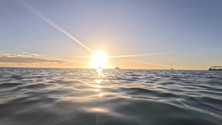 A video short transitions from an underwater view of the sun rays shining through the water's surface, then emerging to show the sunset across the ocean