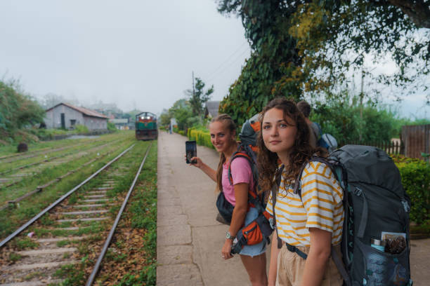 Two women on railway station backpacking in Sri Lanka, one woman photographing train with smartphone