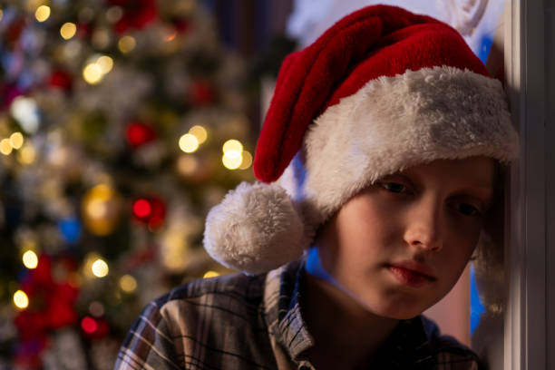 istock Sad boy in Santa hat by Christmas tree 2183695742