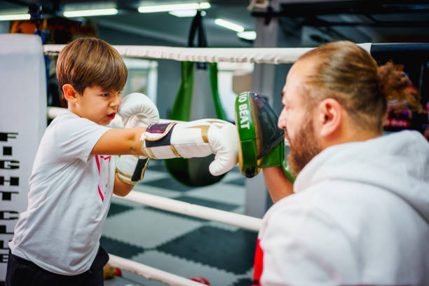Focused young boy practicing boxing with his trainer inside a boxing ring in a gym