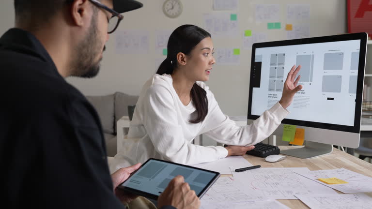 UX UI designers discussing and brainstorming on wireframes for a website and mobile app prototype, surrounded by sketches of user flow and design tools, in the concept of website and mobile application design concept.