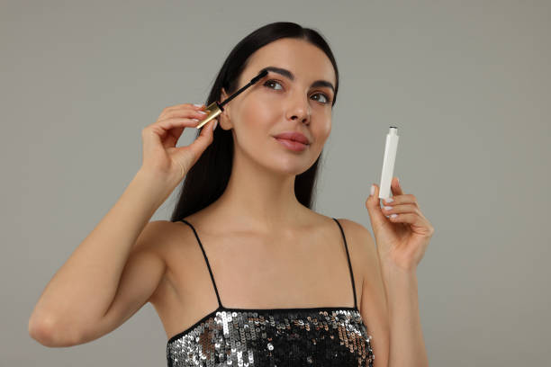 istock Beautiful young woman applying mascara on grey background 2183714047