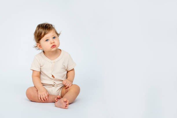 istock A baby boy is sitting on a white isolated background with a place for text in light clothes. A small happy child looks away, space for text 2183717162