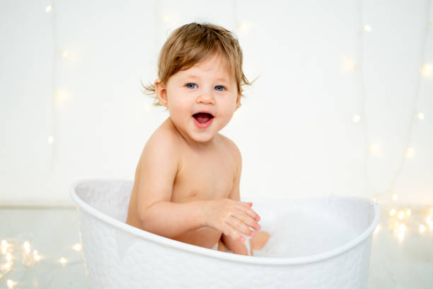 A baby boy is bathing in a bubble bath and playing with rubber ducklings for bathing on a white isolated background with a place for text. A small happy child washes the space for text