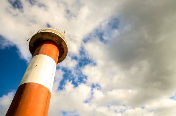 A lighthouse is standing tall in the sky with a cloudy background. The lighthouse is white and red, and it is the only object in the image. The cloudy sky creates a moody atmosphere