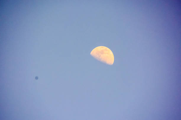 A large moon is in the sky, with a small satellite in the background. The sky is clear and blue, with no clouds in sight