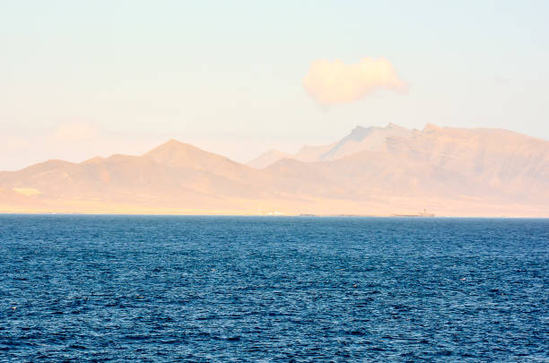 A beautiful blue ocean with a mountain range in the background. The sky is a mix of blue and pink, creating a serene and peaceful atmosphere