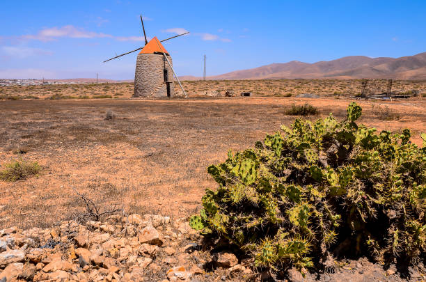 A windmill is in the middle of a desert. The desert is barren and dry. The windmill is the only sign of life in the area