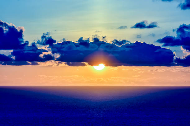 The sky is blue and the sun is setting. The sun is in the middle of the sky and the clouds are scattered