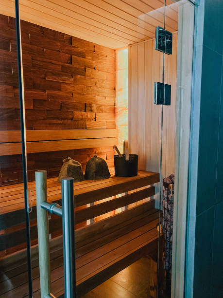 A wooden sauna with a bucket on the bench. Electric steam sauna with glass door.