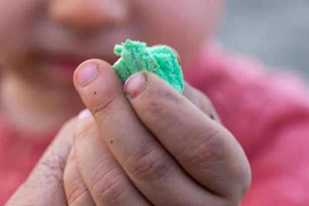 A child is holding a green object in their hand. The object is small and green, and it is a piece of play dough. The child's hand is covered in dirt, suggesting that they have been playing outside
