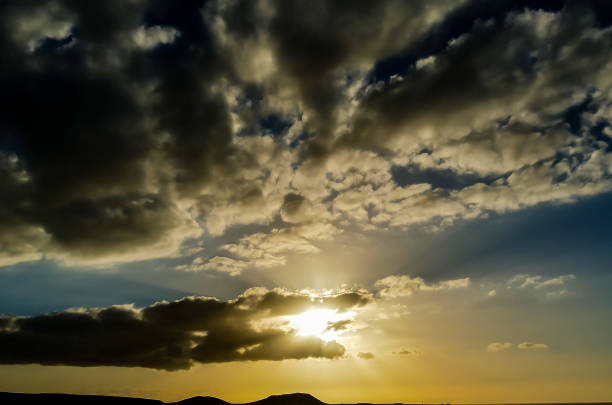 The sky is cloudy and the sun is setting. The clouds are dark and the sky is blue