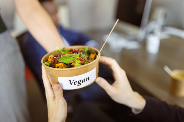 A vibrant vegan lunch bowl being handed over from one person to another in an office setting during daytime.