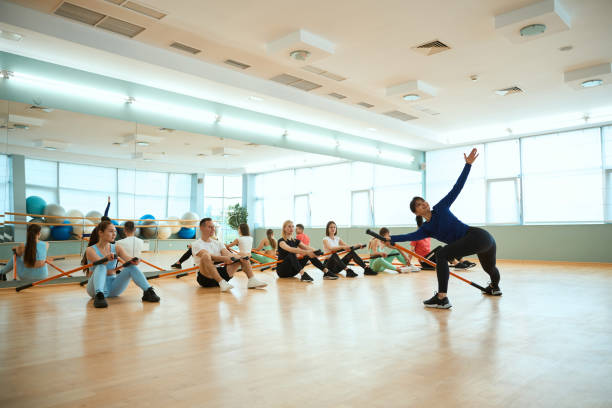 istock Female coach showing for people physical exercises using gymnastic sticks in gym 2183730367