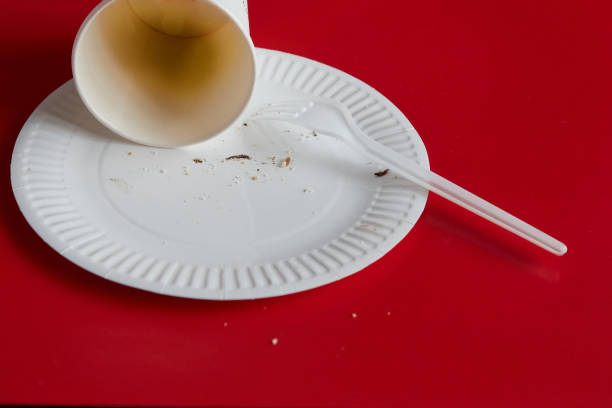 istock Disposable fork with a disposable plate and paper cup alongside a used napkin on a red background, disposable tableware, recycling of waste and raw materials, end of celebration. 2183733920