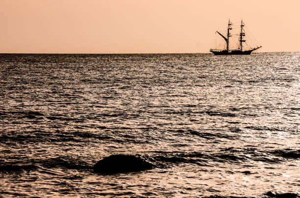A large ship sails in the ocean, with the sun setting in the background. The scene is serene and peaceful, with the ship being the only object visible in the water