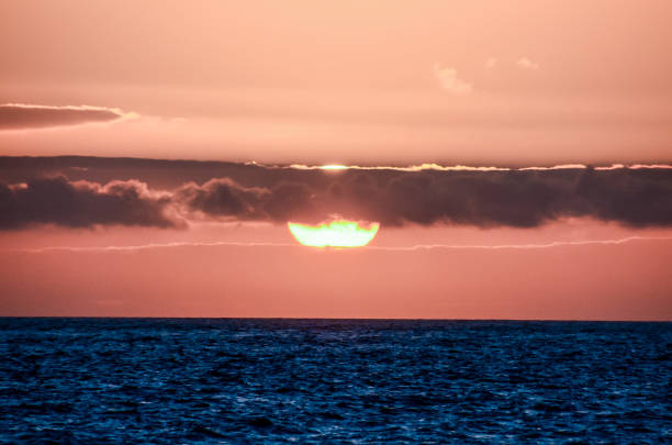 The sun is setting over the ocean, casting a warm glow on the water. The sky is filled with clouds, creating a serene and peaceful atmosphere