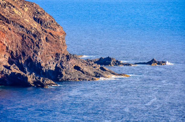 A rocky shoreline with a blue ocean in the background. The rocks are scattered along the shoreline, and the water is calm