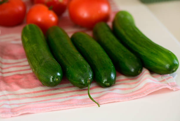 A vibrant display of freshly harvested cucumbers and ripe tomatoes rests on a striped kitchen towel.