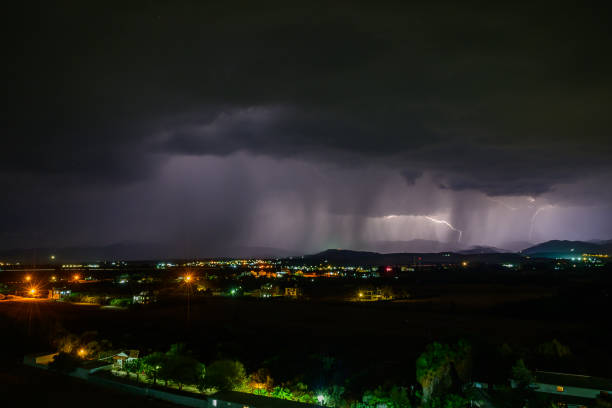 Brilliant flashes of lightning break the night as rain cascades down on a peaceful landscape, captivating the eye.
