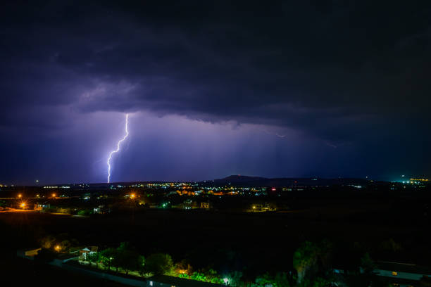 Powerful lightning strike illuminating a dark and stormy night sky. Jagged forks of bright white and blue lightning streak across the frame, originating from a bright flash within the turbulent, dark rain clouds. Heavy rain is visible as streaks across the image, emphasizing the intensity of the thunderstorm. The overall mood is one of raw power and the formidable forces of nature.