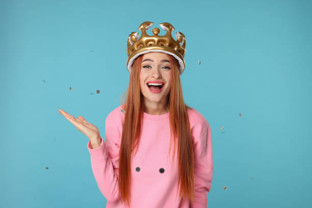 istock Beautiful young woman with inflatable crown under falling confetti on light blue background 2183746741