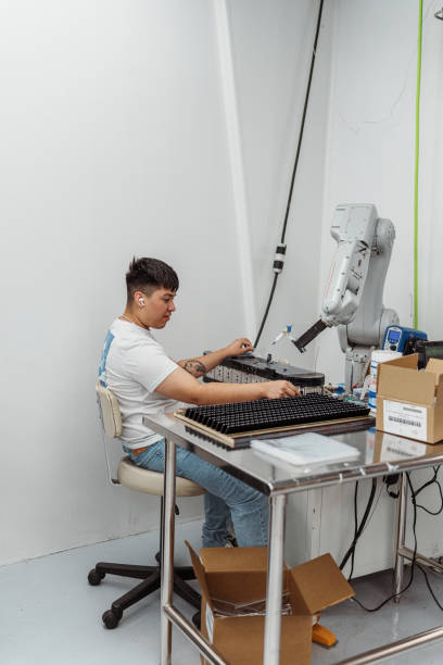 A young male worker of Latin American descent operates a robotic arm when working in a manufacturing and fabrication facility.