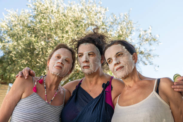 Portrait of three women outdoors with collagen mask on their faces against flowering olive tree.