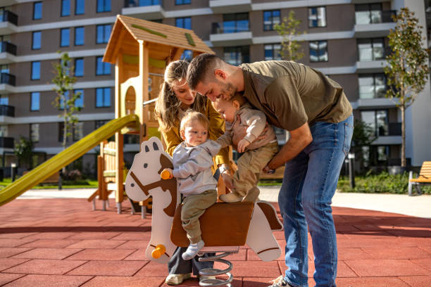 Parents helping twin baby boys to rock on horse on the playground on sunny day