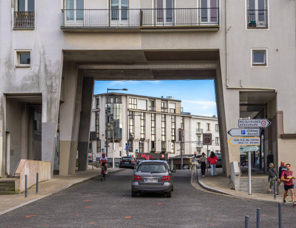 Brest, France - July 24, 2024:A modern urban scene in Brest featuring a street passing through a large architectural archway. Cars and cyclists navigate the road, with buildings on either side.