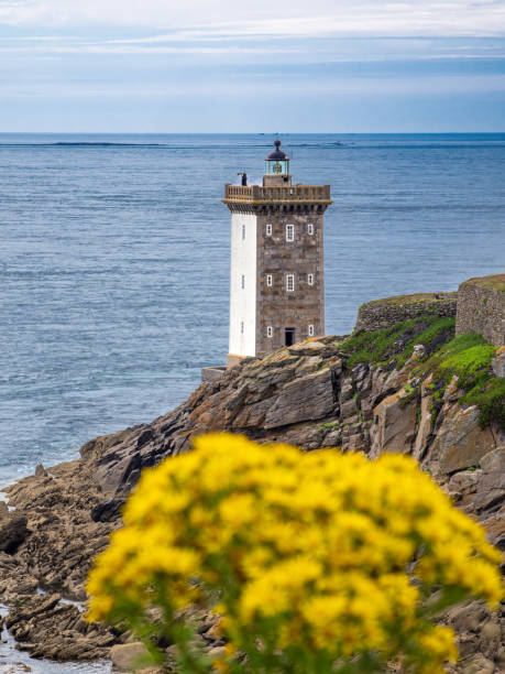 A scenic coastal panorama featuring a lighthouse Phare de Kermorvan on rocky terrain and blurred yellow flower foreground