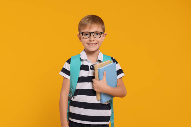 istock Happy schoolboy in glasses with backpack and books on orange background 2183761749