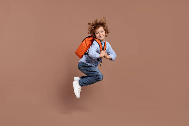 istock Happy schoolboy with backpack jumping on brown background 2183761826