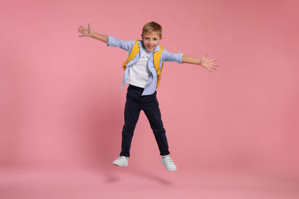 istock Happy schoolboy with backpack jumping on pink background 2183761879