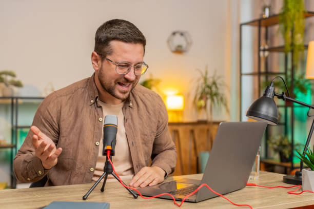 istock Happy young Caucasian man influencer speaking into microphone and laptop webcam at home office table 2183772041