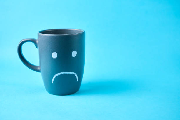 istock A coffe cup with a sad face, on a plain blue background, Blue Monday concept. 2183785723
