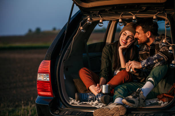 istock Young couple in love sitting in car open trunk 2183804367