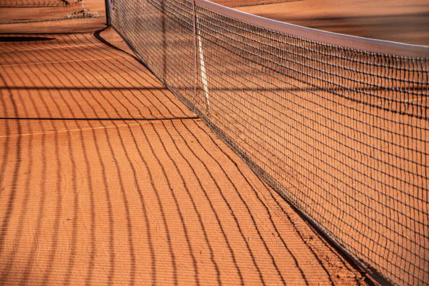 Tennis court net with shadow on the red clay sand. Sports background.