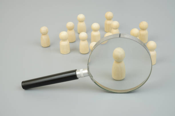 istock Wooden figures and magnifying glass on gray background. 2183820230