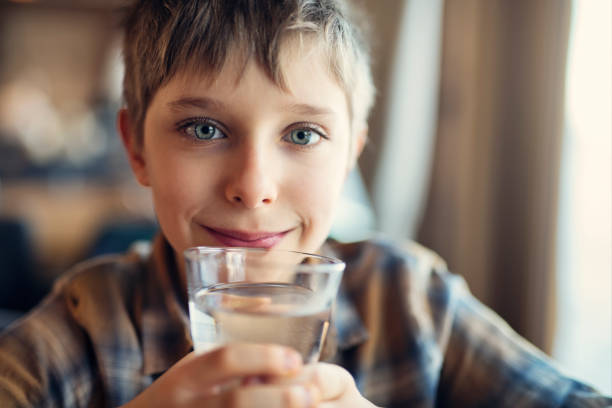 Portrait of a cute little boy drinking a glass of tap water. The boy is 9 years old and he is smiling at the camera.Shot with Nikon D850