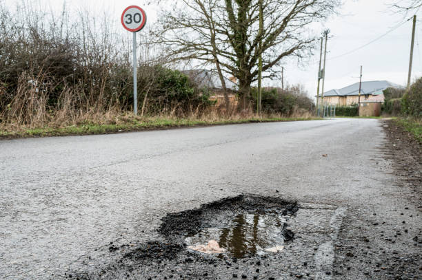Deep and dangerous pothole seen on a typical British rural road which causes damage to vehicle wheels. stock photo