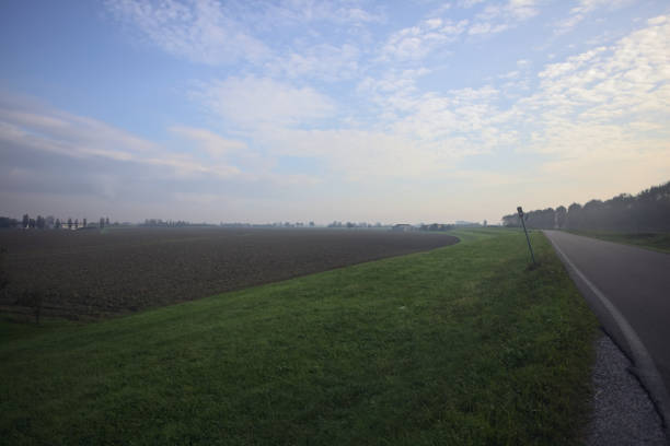Country road over an embankment next to a ploughed field on a cloudy day